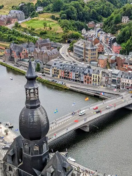 An aerial shot of the cityscape of Dinant, Belgium, with a bridge over the river Meuse and lush trees in the background