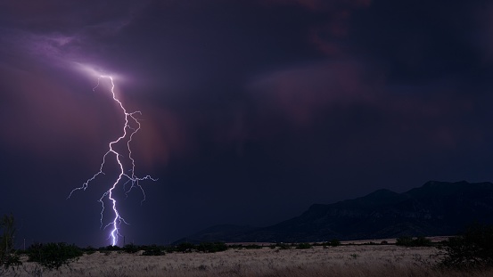 The lightning strikes in the evening blue sky over the mountains covered with trees