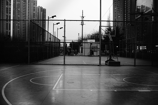 A grayscale shot of an empty basketball court with buildings in the background