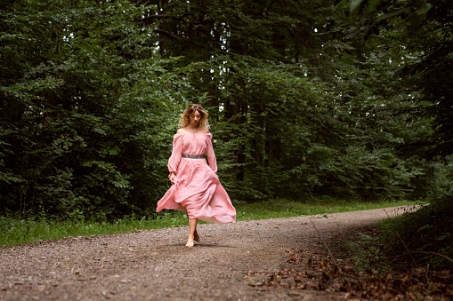 A Pretty blonde female in a pink dress walking on a path in the forest