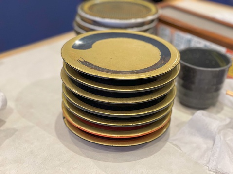 A large stack of empty plastic gold-colored sushi plates with a plastic grey key cup at a conveyer belt sushi restaurant in Kasukabe, Saitama, Japan.