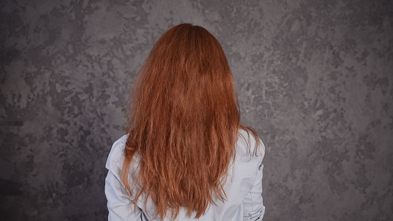 A young ginger hair girl standing facing the gray wall