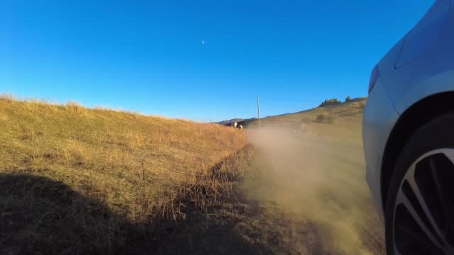 Car wheel spinning on mountain dirt road and sunset lights streaming POV