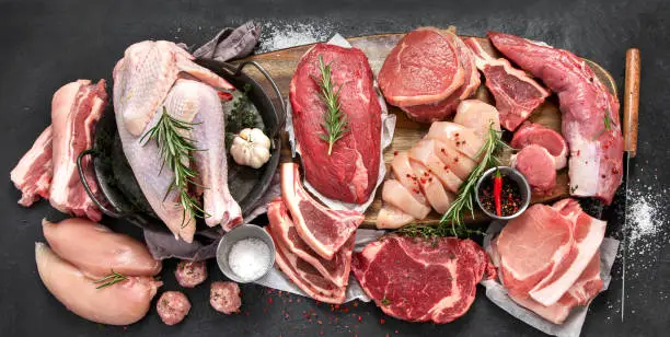 Different types of raw meat - beef, pork, lamb, chicken on dark background. Top view, copy space