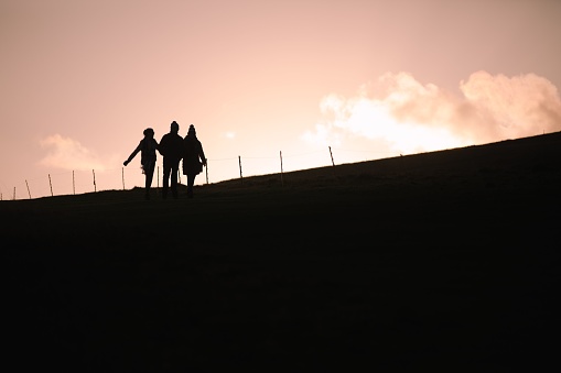 Three people in silhouette walking along the top of the South Downs, East Sussex, UK