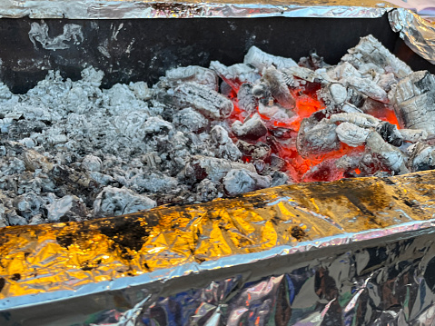 Stock photo showing close-up, elevated view of a pile of red hot charcoal embers and ash in metal barbecue tray full to heat for barbecue cooking. These hot coals have stopped smoking and are now glowing orange, indicating that they are ready to be spread out.