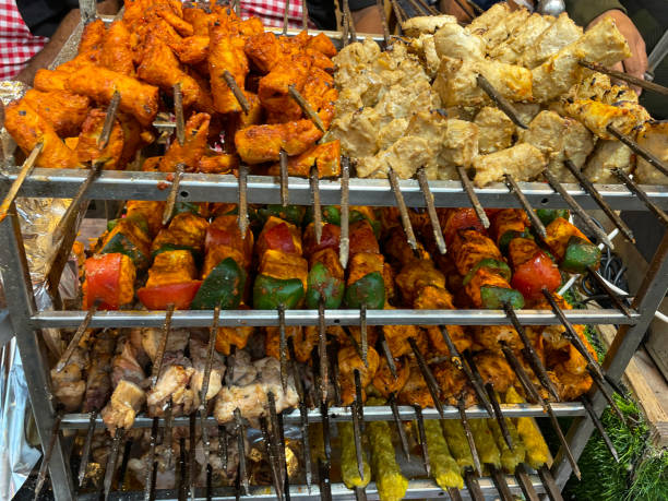 Close-up image of food stall shelving rack display of chicken and vegetable kebabs, chicken breast pieces chargrilled and skewered with onion, red and green peppers, covered in spicy sauce, elevated view, focus on foreground