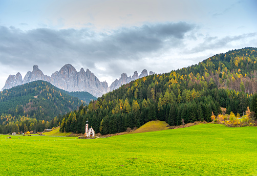 The small and beautiful church of Saint John, Ranui, Chiesetta di san giovanni in Ranui Runes South Tyrol Italy, surrounded by green meadow, forest and Dolomite mountains