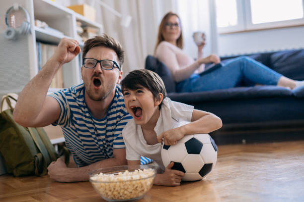 istock cheerful father and son watching soccer game at home 1443194738