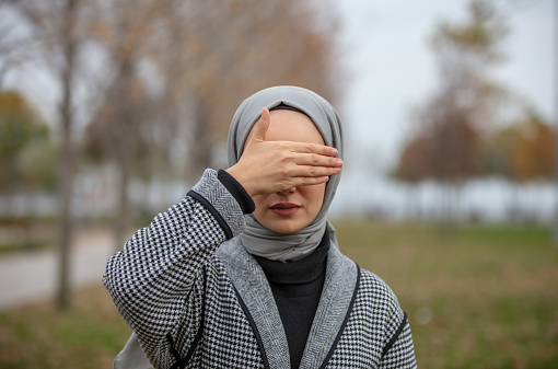 Hijab girl covers her face with her hand.
A girl in a beautiful dress and in public park.