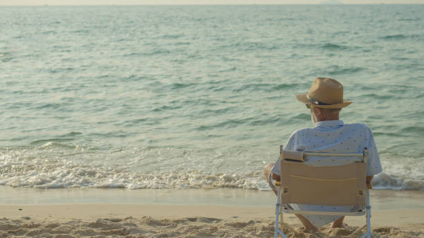 elderly men sit chair at the beach watching the sun and the sea on their summer vacation and they smile and enjoy their vacation. stock photo
