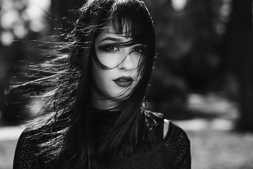 A Portrait of a pretty female in a gothic style looking at camera in the park, grayscale shot