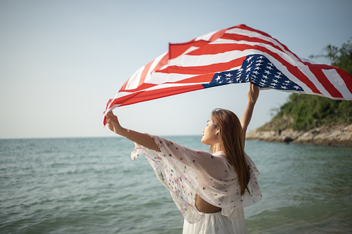 young women hold American flags on the beach and the sea on their summer vacation and they smile and enjoy their vacation.