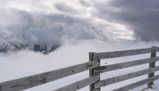 A snowy scene looking over a weathered fence as clouds close in on the mountains at the Cardrona Alpine Ski Resort on South Island New Zealand in August 2003.