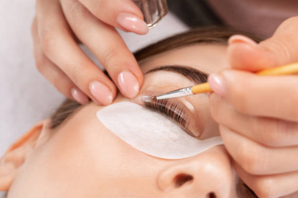 make-up artist makes the procedure of lamination and dyeing of eyelashes to a beautiful woman in a beauty salon. eyelash extensions. eyelashes close-up - oppakken stockfoto's en -beelden