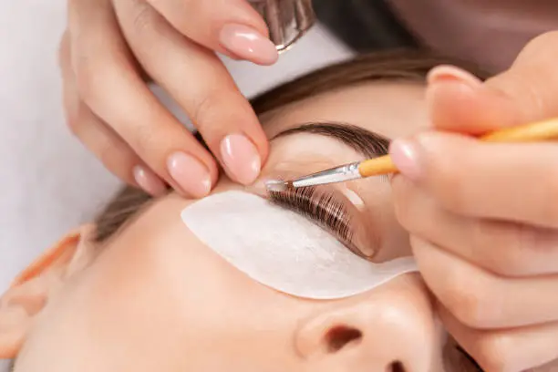 Photo of Make-up artist makes the procedure of lamination and dyeing of eyelashes to a beautiful woman in a beauty salon. Eyelash extensions. Eyelashes close-up