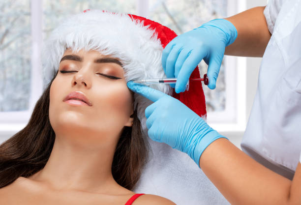 die kosmetikerin macht anti-aging-anti-falten-injektionen auf das gesicht einer schönen frau in einem roten weihnachtsmannhut. ästhetische kosmetik für frauen in einem schönheitssalon. neujahrskonzept. - plastic surgery botox injection face lift nose job stock-fotos und bilder