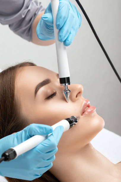 A doctor cosmetologist makes a microcurrent facial therapy to a young woman with a device in a beauty wellness salon.Cosmetology and professional skin care. stock photo