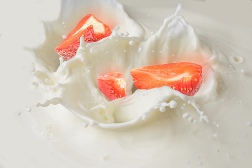 Splash from the falling strawberry in milk, lifting milk drops
