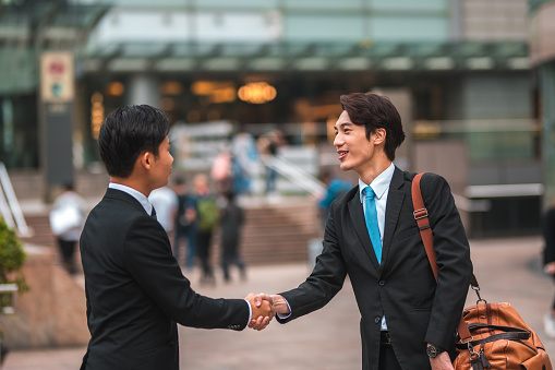 Outdoor shot of two asian employees shaking hands in the streets of Hong Kong. Businessmen greeting.