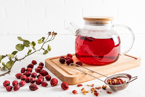 a large glass teapot on a wooden board and a white background with vitamin tea from rose hips. increased immunity. anti-inflammatory effects