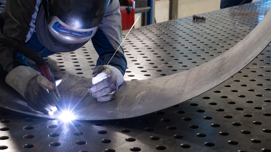 Male welder wearing helmet working with welding torch in factory.