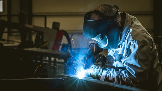 The welder performs welding task at his workplace in the factory, while the sparks \