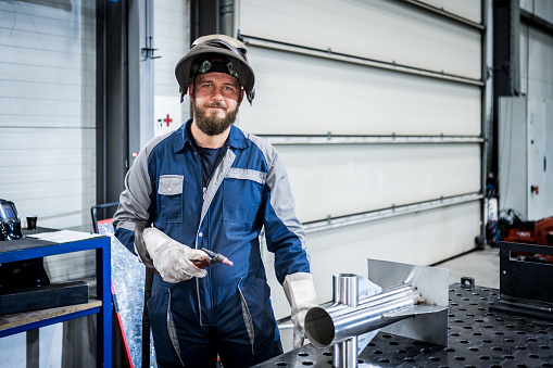 Portrait of male welder holding welding torch in factory.