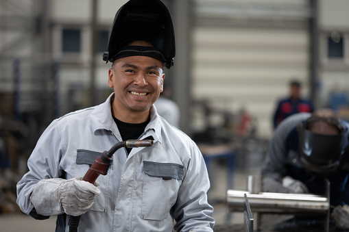 Portrait of smiling male welder holding welding torch in factory.