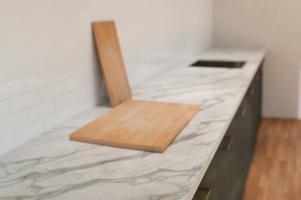 istock White and grey kitchen, white marble countertop with wooden cutting board. Grey cabinets, white tile. 1443211307