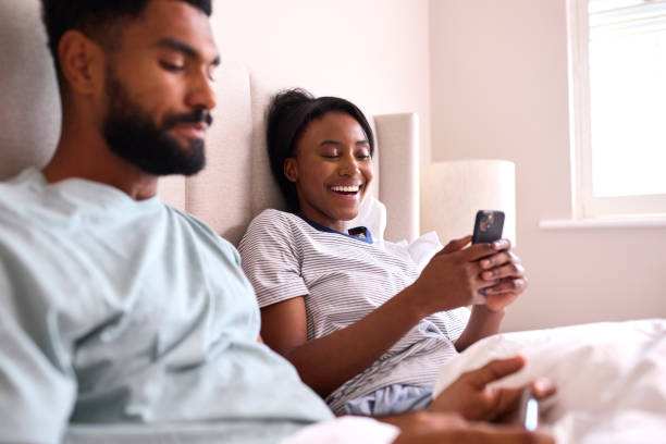istock Young Couple At Home Both Looking At Mobile Phones In Bed Together 1443211397
