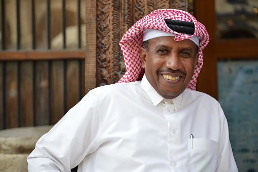 Smiling local businessman in traditional arabic clothing having a relaxed break on a sunny day in downtown Doha, Qatar