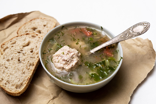 Vegetable soup with meatballs in a plate on a white background. Two slices of bread side by side.