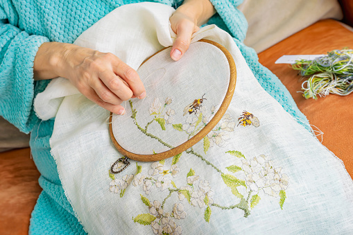 Hands of senior woman making embroidery in wooden embroidery hoop on sofa