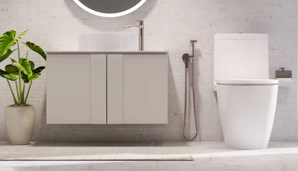Modern and luxury design bathroom with beige vanity, white ceramic sink, toilet bowl, stainless steel bidet sprayer, toilet paper roll hanger and potted plant in dappled sunlight from window granite wall and marble floor for cleaning, toiletries product display background baño de diseño moderno y de lujo con tocador beige, lavabo de cerámica blanca, inodoro, pulverizador de bidé de acero inoxidable, percha de papel higiénico y planta en maceta a la luz del sol moteada de la pared de granito de la ventana y el piso de m