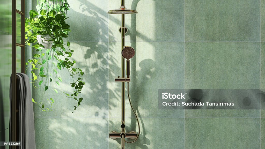 Modern and luxury bathroom design with shiny gold colored rain shower, shower head on slide bar on beautiful green granite wall and creeper plant with sunlight from window Modern and luxury bathroom design with shiny gold colored rain shower, shower head on slide bar on beautiful green granite wall and creeper plant with sunlight from window for home interior decoration, architecture and design background Bathroom Stock Photo