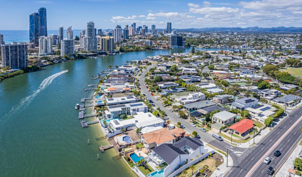 Aerial view Nerang River Housing estate (Isle of Capri) with Surfers Paradise and Pacific Ocean Aerial view Nerang River Housing estate (Isle of Capri) with Surfers Paradise and Pacific Ocean in the background. In the centre frame a speedboat (private craft) creates a wake in the river. Luxury waterfront houses with swimming pools, private boat moorings & piers. 16x9 panorama format. queensland stock pictures, royalty-free photos & images