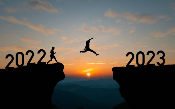 Silhouette man jumping from 2022 cliff to 2023 cliff with cloud sky and sunlight and happy new year in 2023 in Concept of start a business stock photo