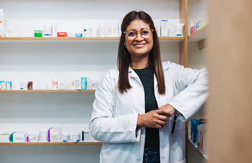 Female pharmacist standing in a drug store and looking at the camera. Happy woman working in a pharmacy. Portrait of a female healthcare worker in a chemist.