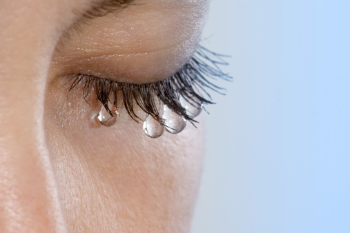 Woman's eye with several teardrops hanging on her eyelashes