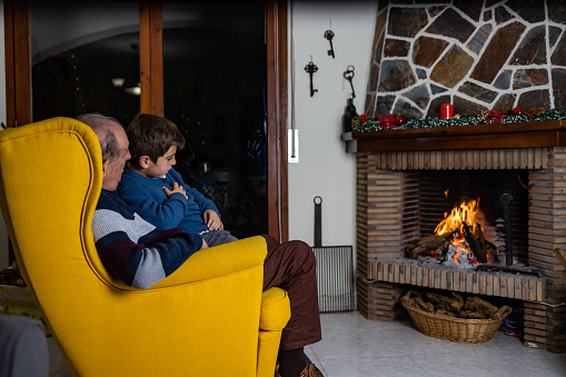 Senior man and his grandson sitting in front of the fireplace