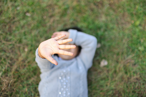 Little Girl Lying and Occlusion face with Palm on Back on the Grass