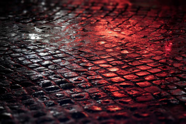 Detail of a street in downtown Rome, Italy, paved with cobblestone after a rainy night, illuminated by white and red lights.
