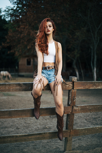 Beautiful young woman with curly red hais is posing on farm.