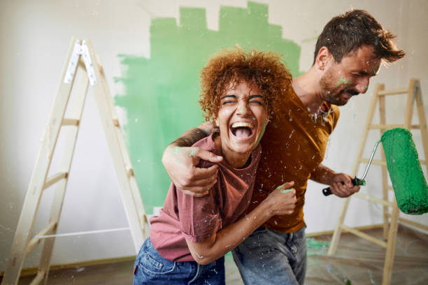 coppia allegra che si abbraccia mentre dipinge la loro nuova casa. - home addition home improvement paint decorating foto e immagini stock