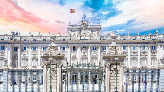 Madrid, Spain - July 19, 2022: Facade of an old gated government building. A flag is flying on the roof of the building, and incidental people are walking on the scene.