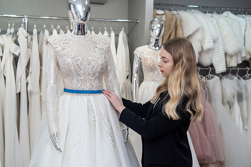 Designer woman's doing measurements elegant wedding dress in store