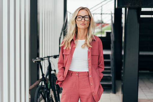 Portrait of an elegant blonde confident woman in glasses standing and looking at the camera