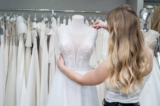 la mariée regarde et touche des robes de mariée blanches tout en étant dans le salon de mariage - wedding bride buying caucasian photos et images de collection