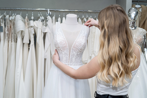 pretty bride look and touch white wedding dresses while being in the wedding boutique